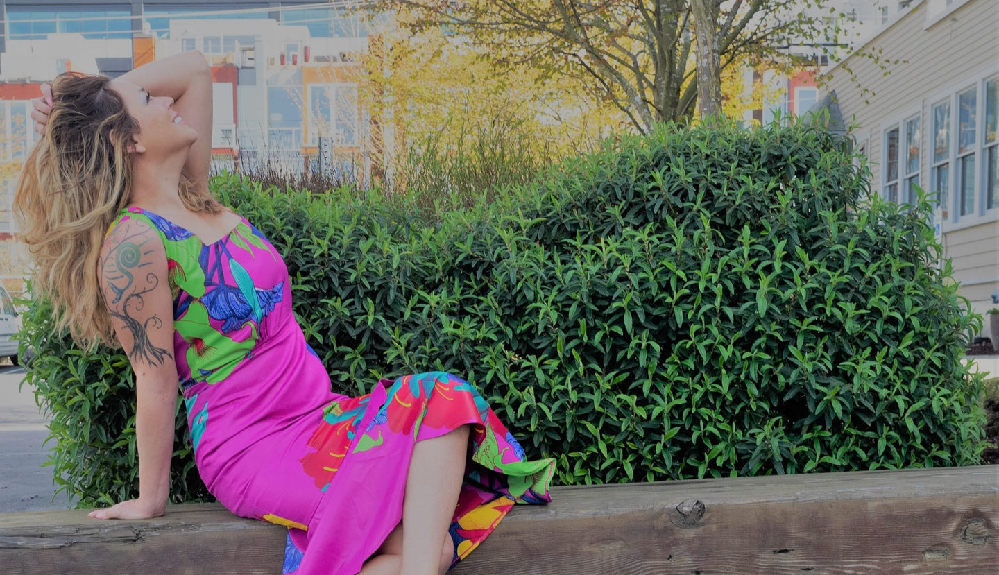 Latina woman posing on a bench, wearing a pink Prima Dona dress with floral accents