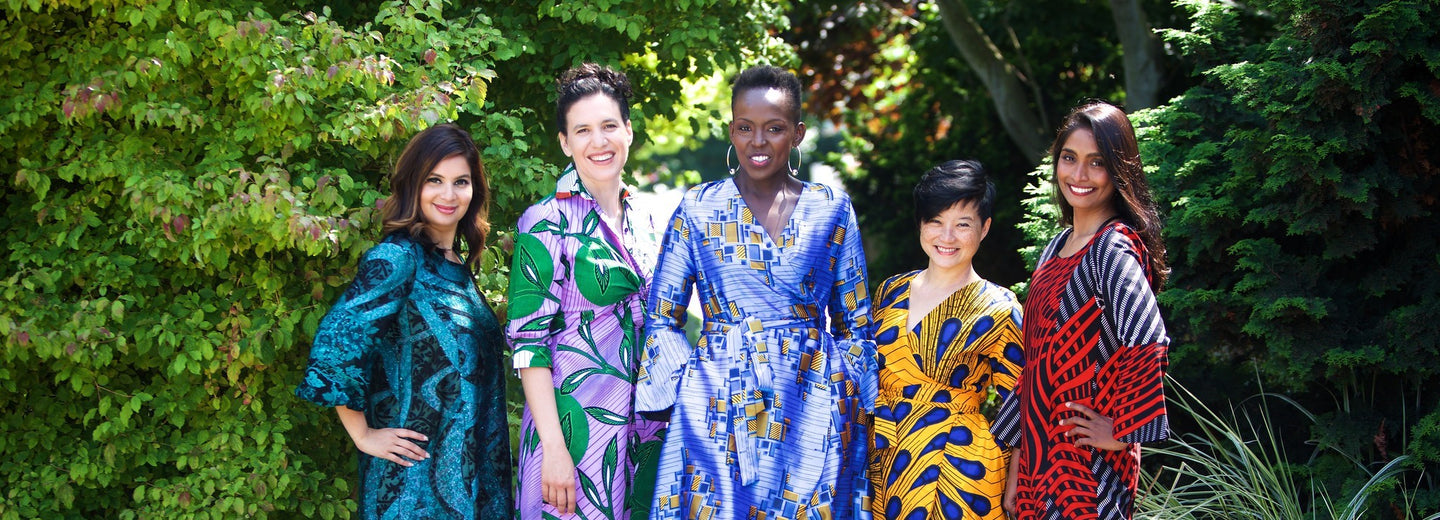 5 women standing wearing Prima Dona dresses with greenery in the background