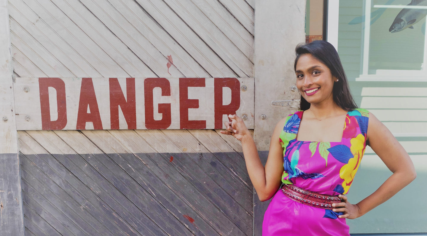 A brown-skinned woman wearing a pink dress standing next to a sign that says DANGER